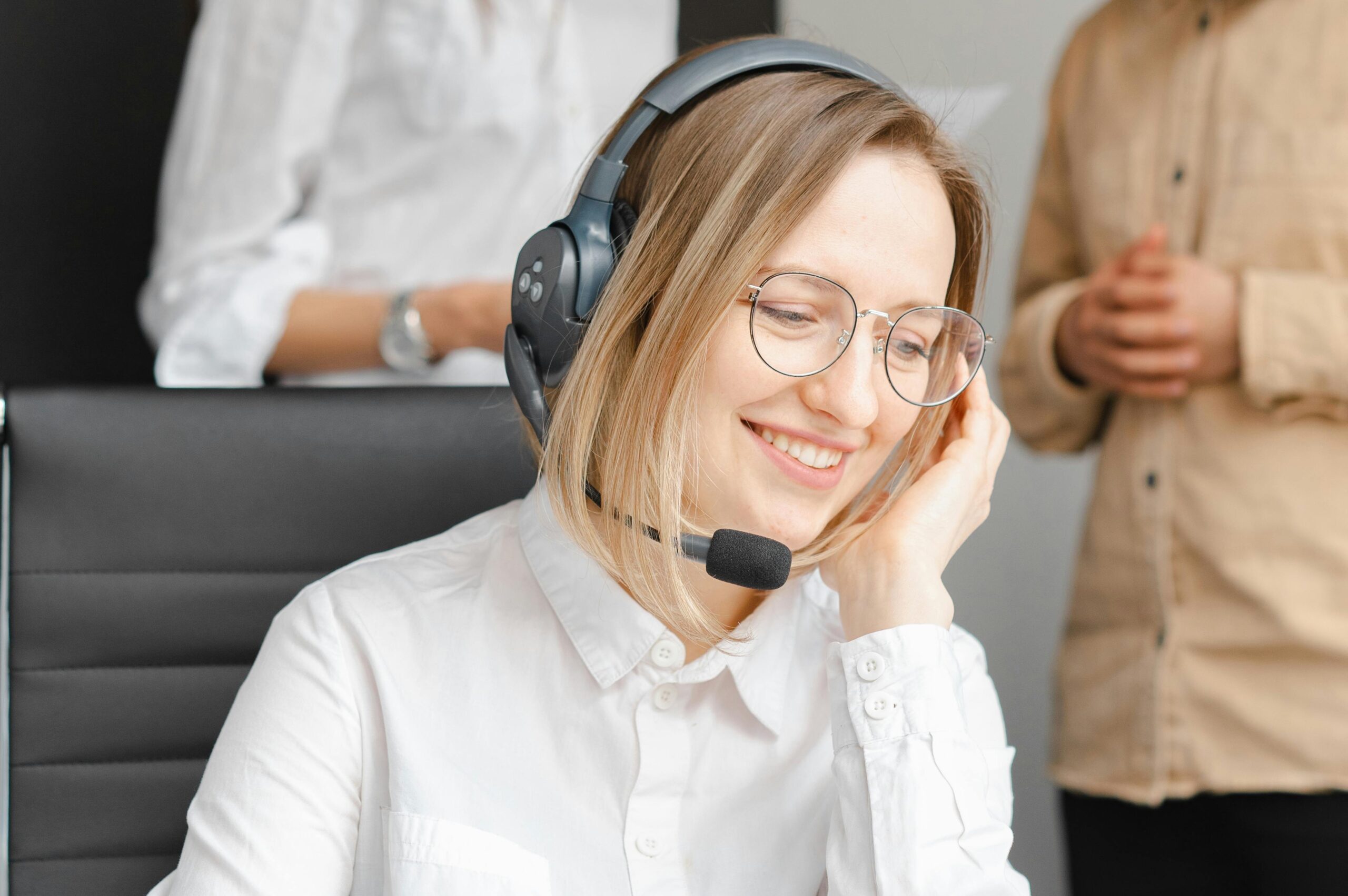 A cheerful woman working at a call center, wearing a headset and glasses, providing excellent customer support.
